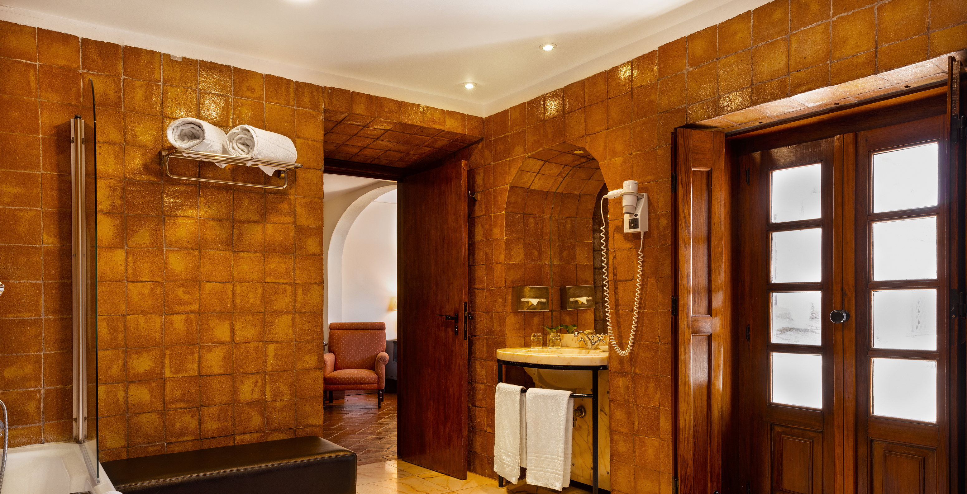 The Superior Family of The Pousada Convento Vila Viçosa has a bathroom in earth tones, with a sink and a bench