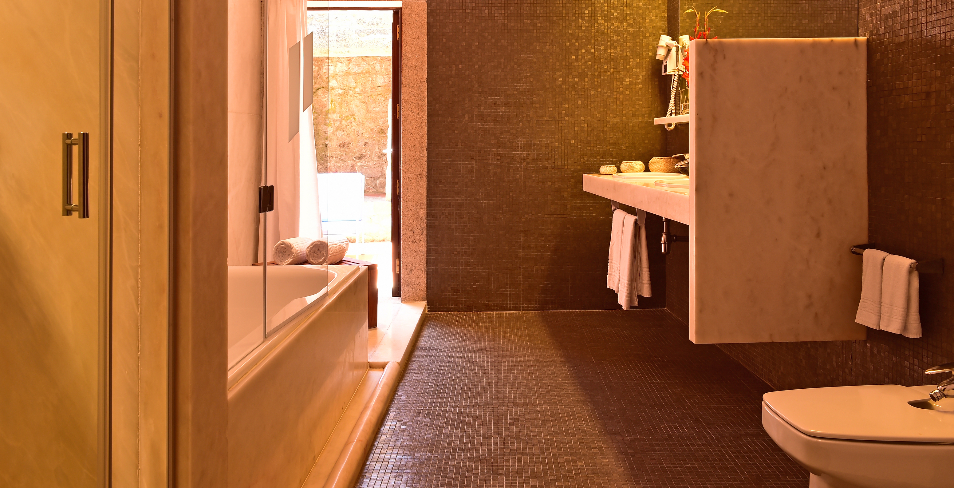 The Master Suite of The Pousada Mosteiro Crato has a bathroom with black tiles, a bathtub, bidet, and two sinks