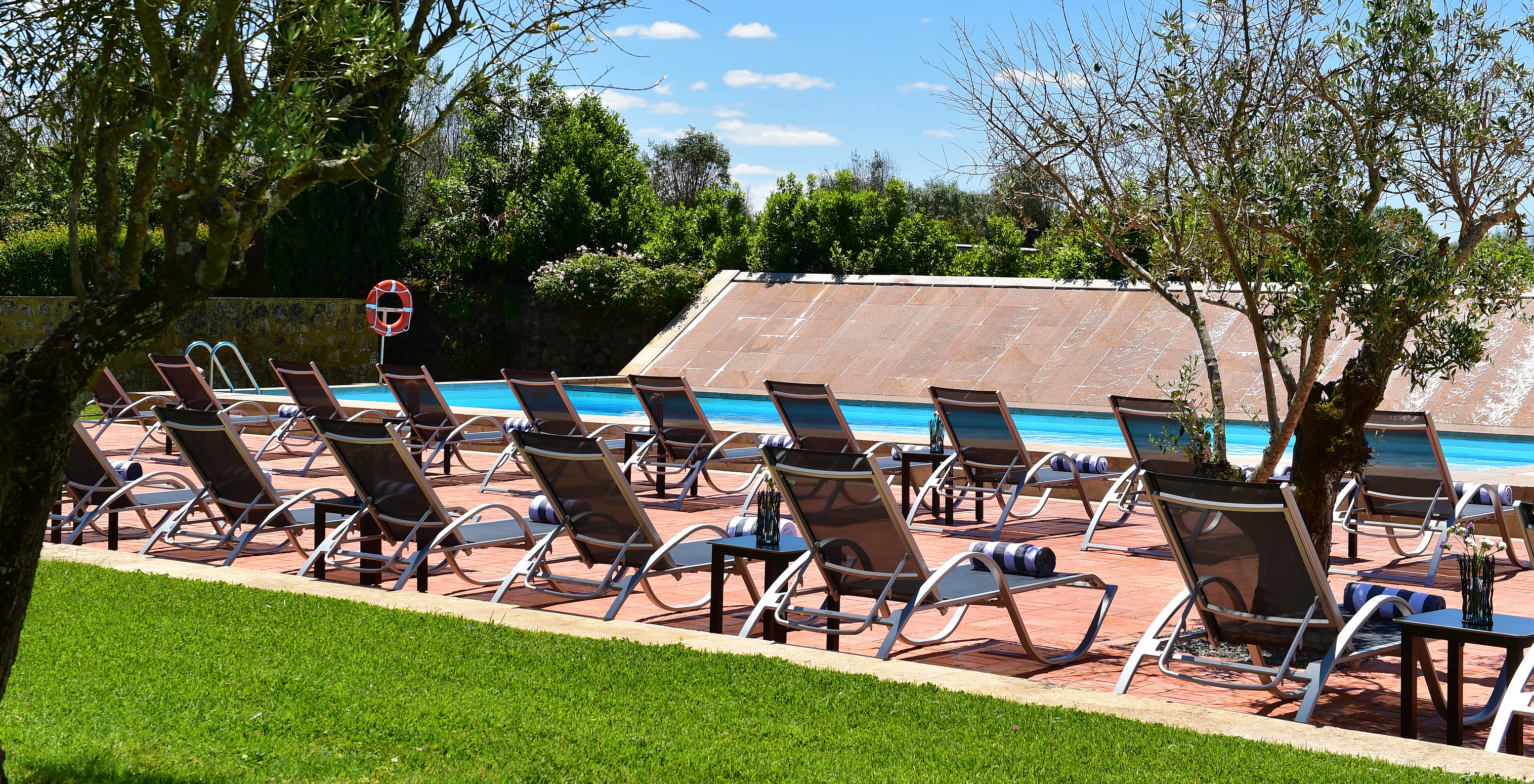 Outdoor pool area with sun loungers for relaxing and sunbathing, surrounded by gardens and trees