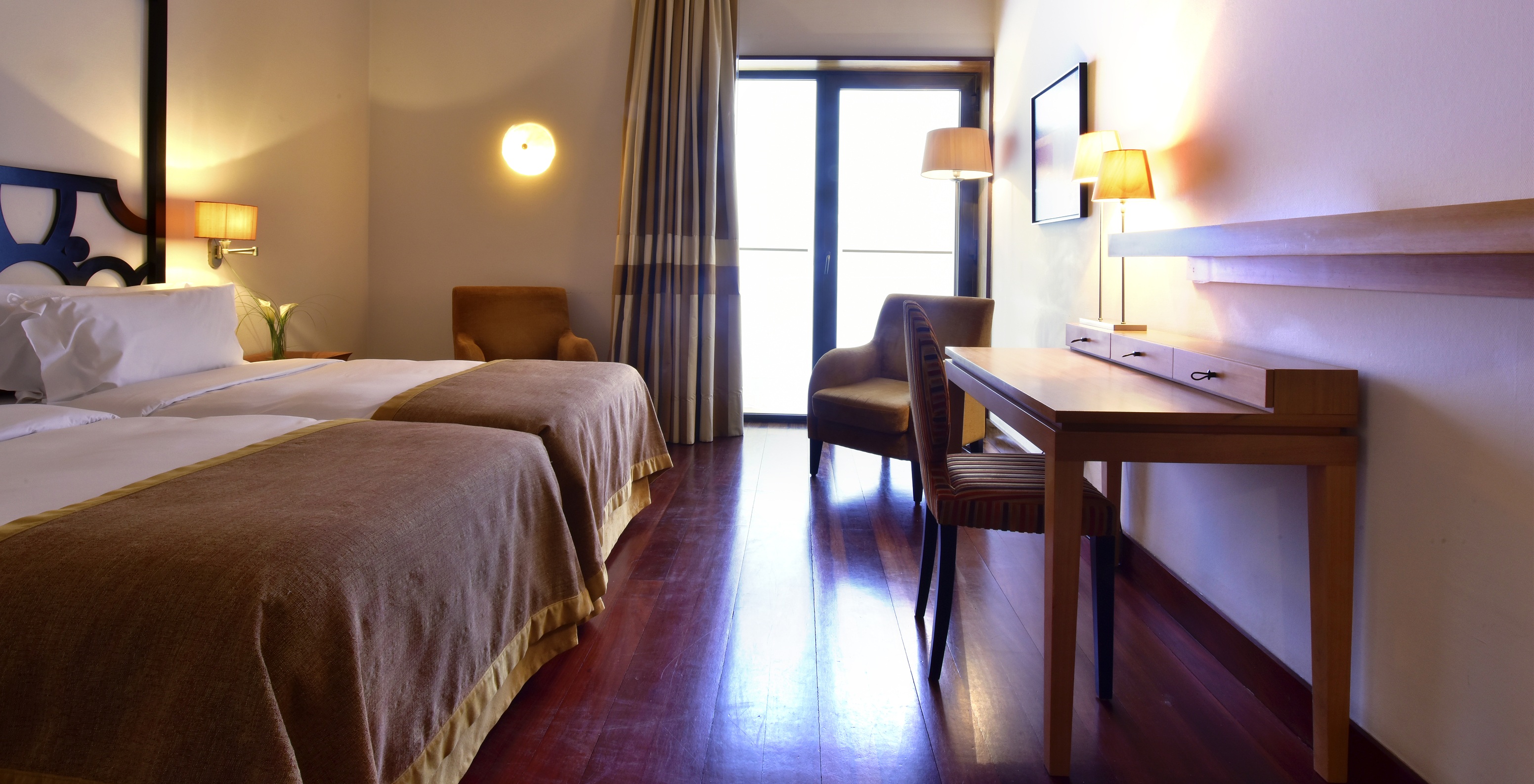 The Superior Room of The Pousada Convento Tavira has two beds, a desk, armchair, and a window with an exterior view