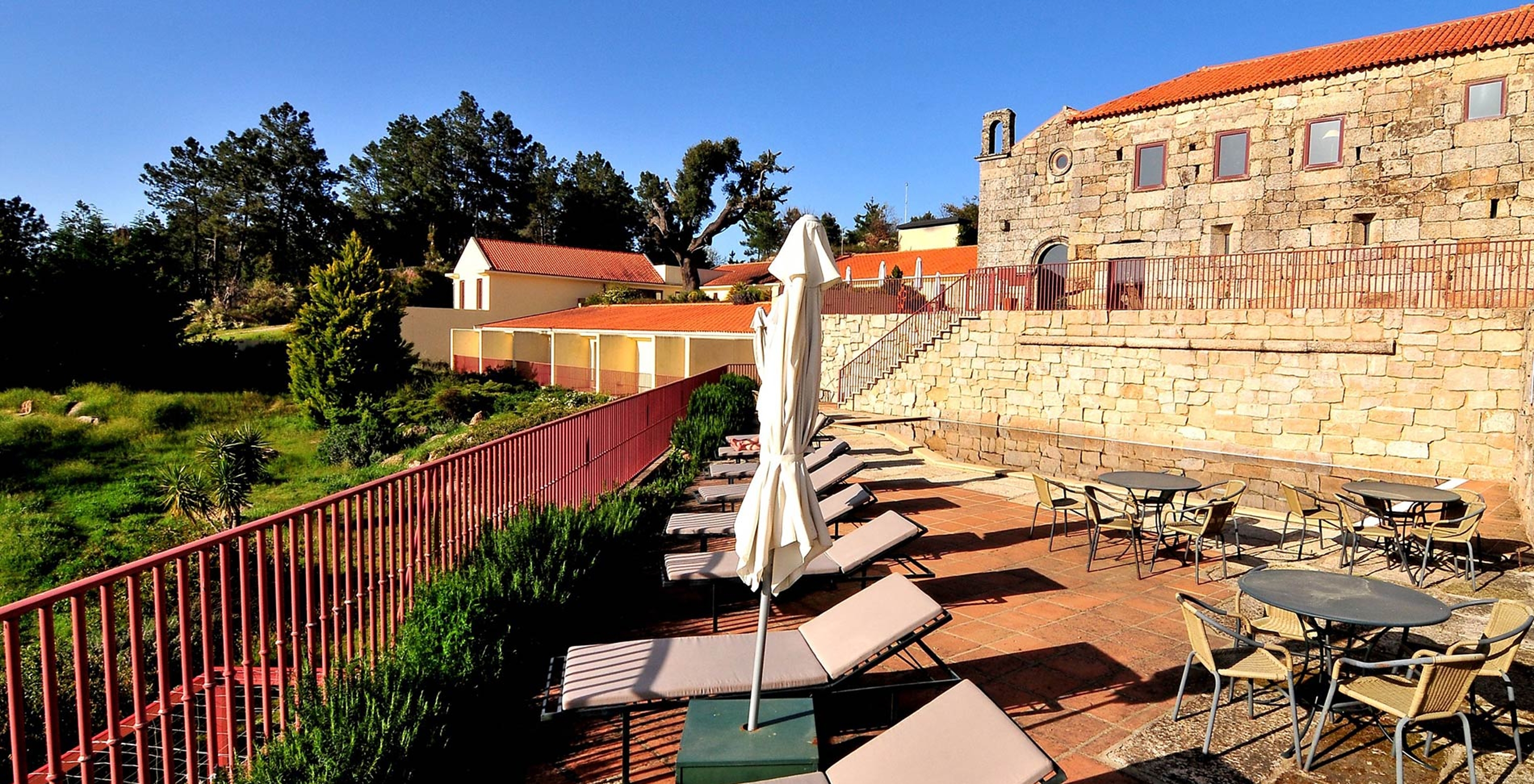 View of the outside of the historic hotel with pool in Belmonte, with stone building, sun loungers, tables, and chairs