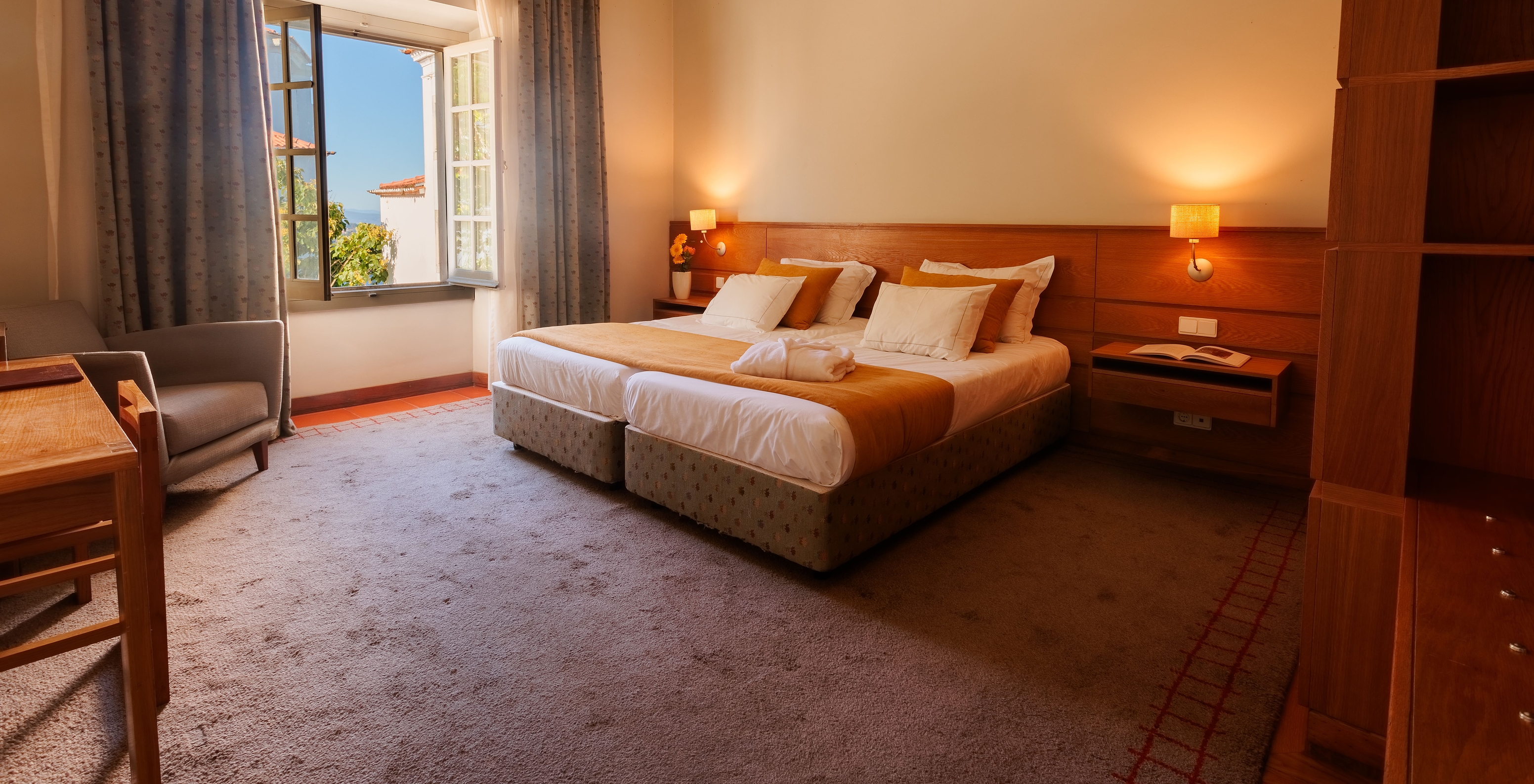 The Suite of The Pousada Ourém features a double bed with an orange bedspread and an open window beside it