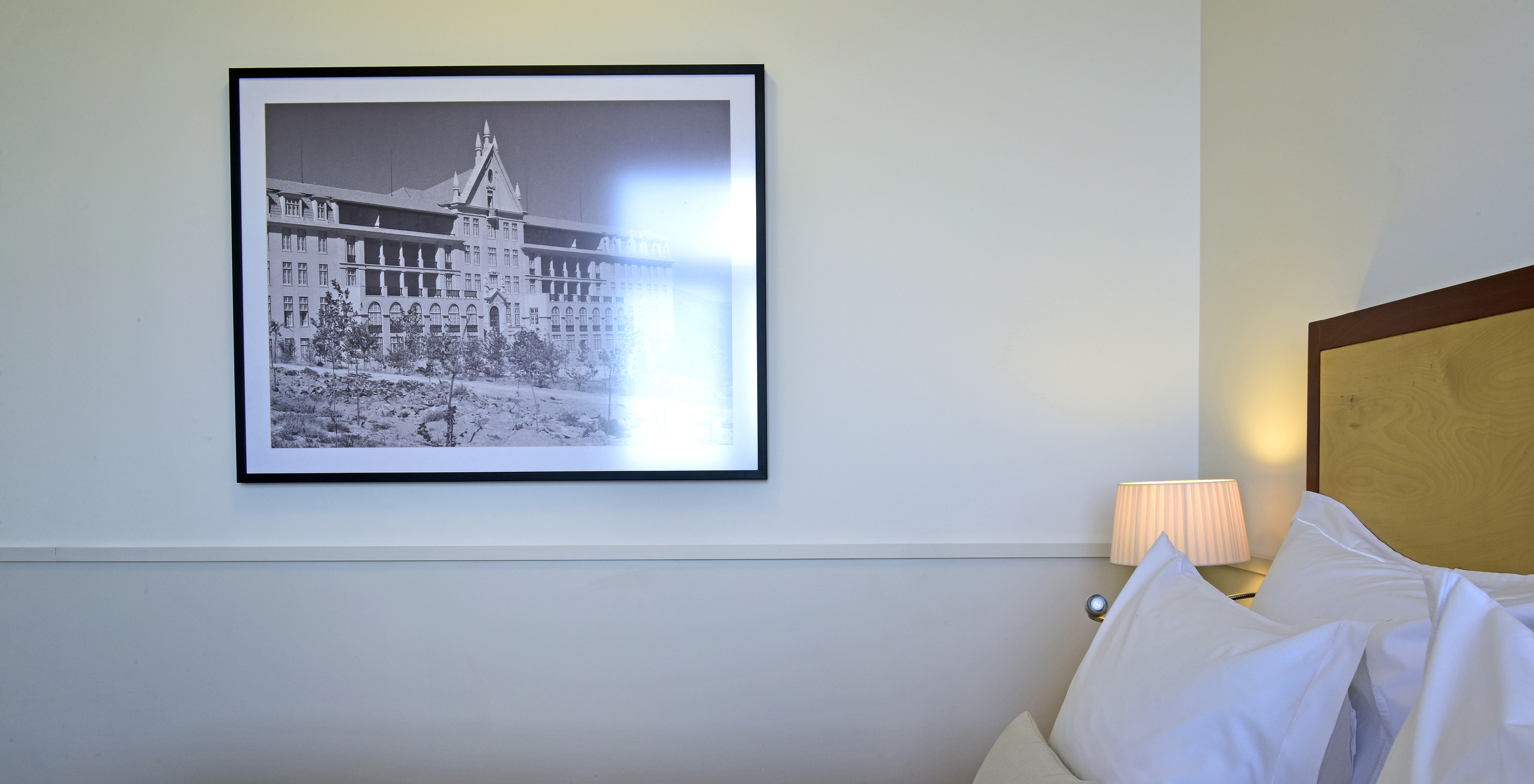 The Classic Family Room of The Serra da Estrela Inn has a double bed with a wooden headboard and a painting of the sanatorium