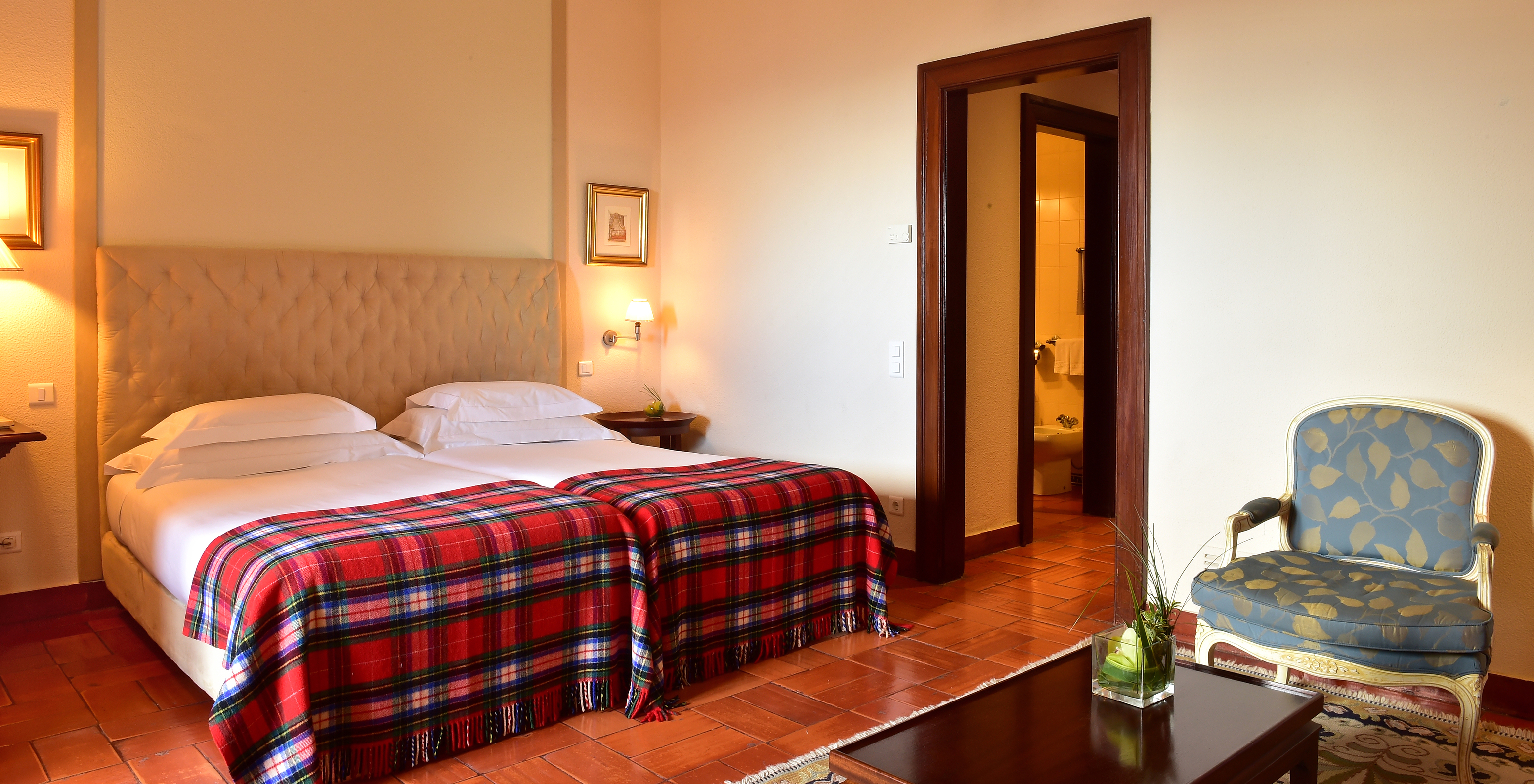 The Superior Family Room at Pousada Castelo Palmela has two beds with a red checkered blanket, bedside table, and armchair