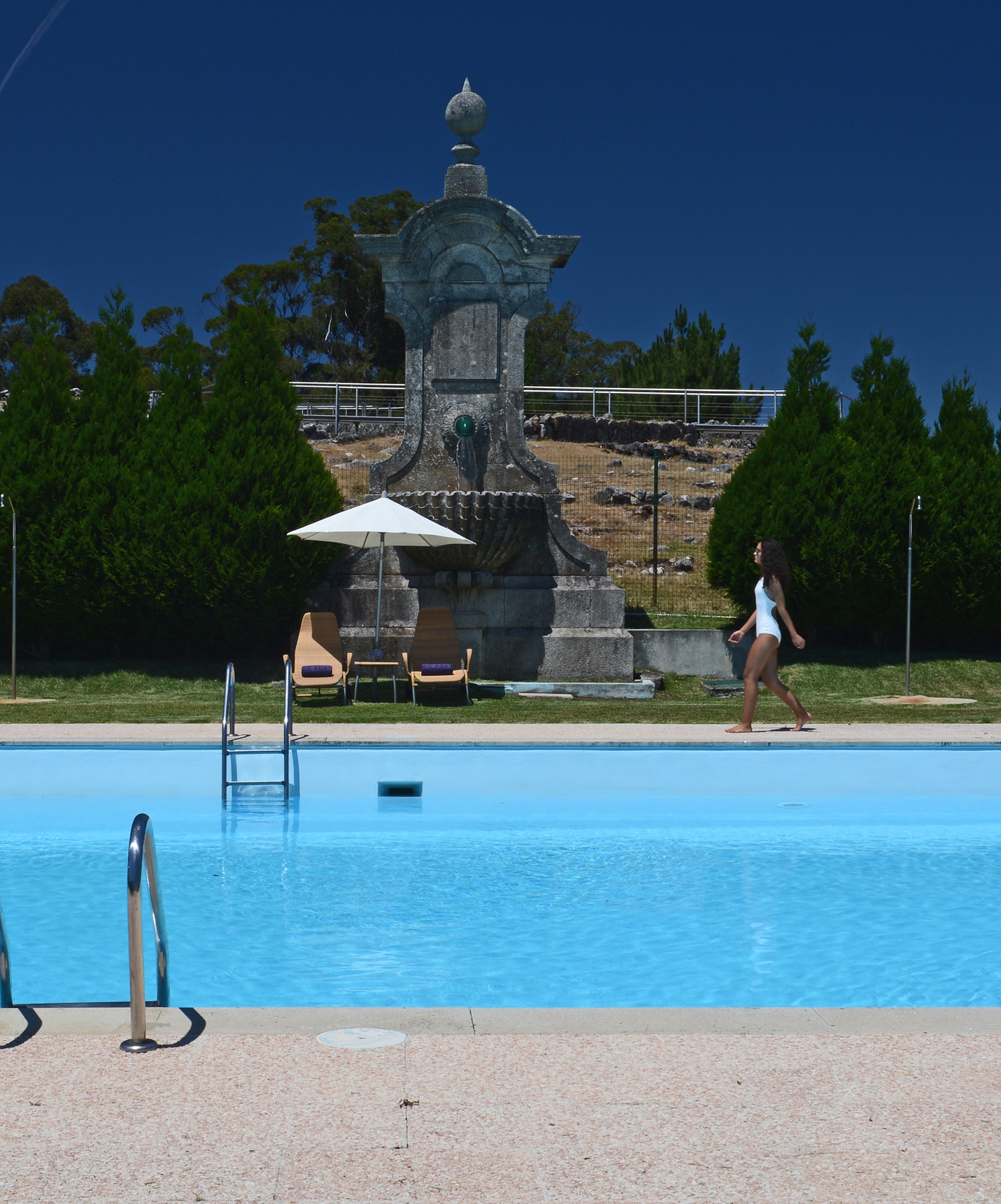 Girl walks beside the outdoor pool at the hotel in Monte de Santa Luzia in a white swimsuit