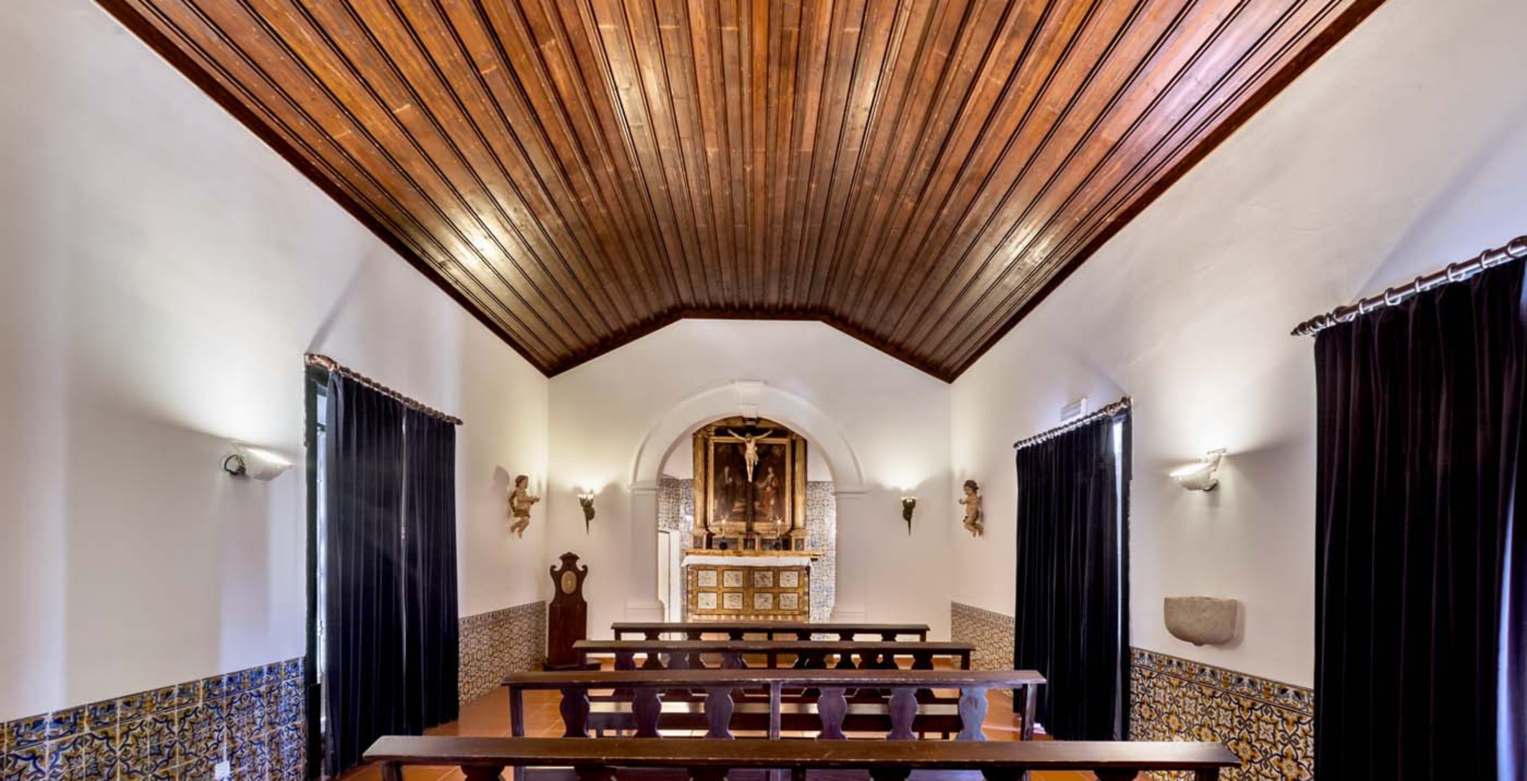 Capilla con techo de madera y tres ventanas con cortinas negras en la Pousada Castelo Alvito, Hotel en Alvito