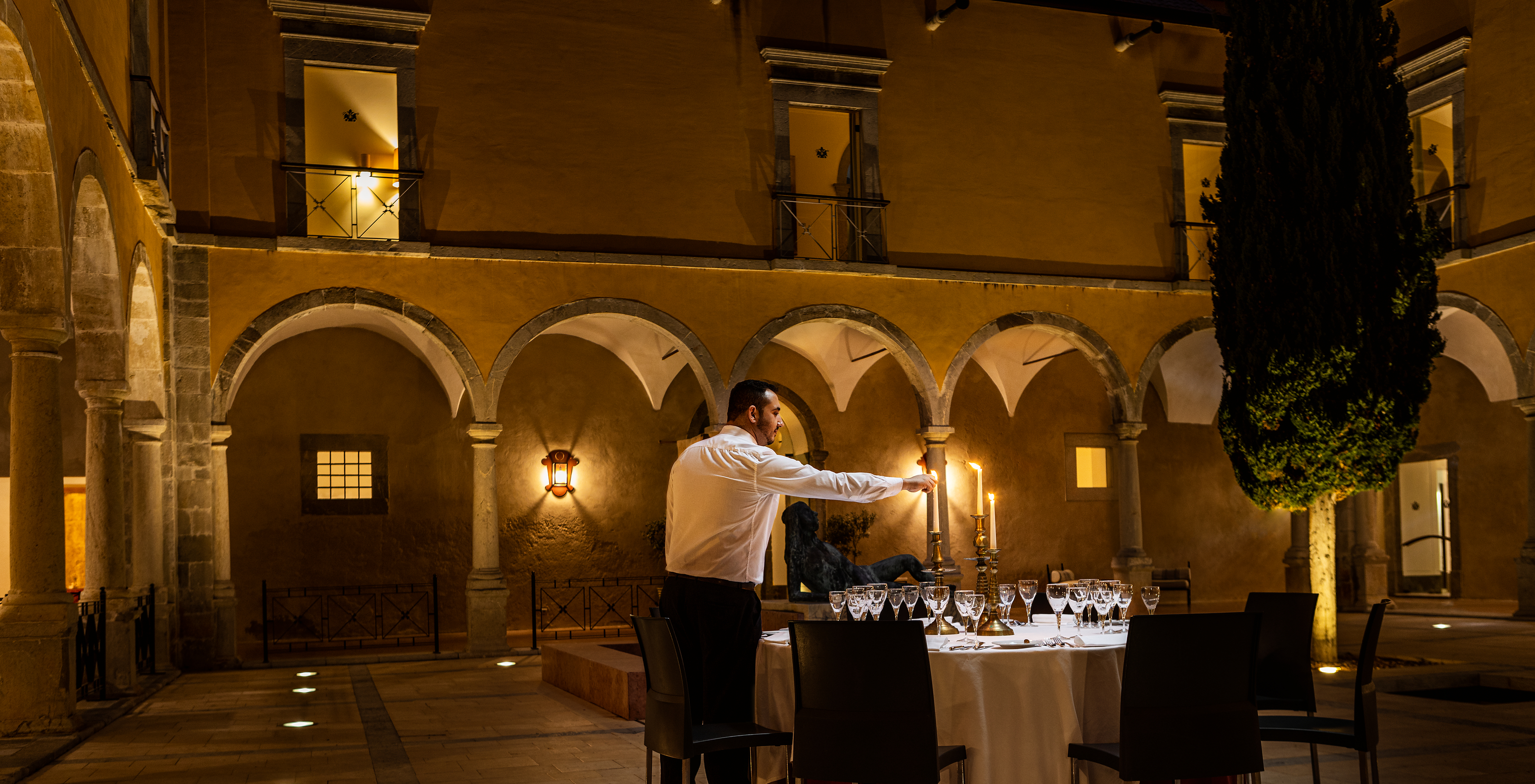 Empleado encendiendo velas en una mesa para cenar en el Claustro de la Pousada Convento Tavira