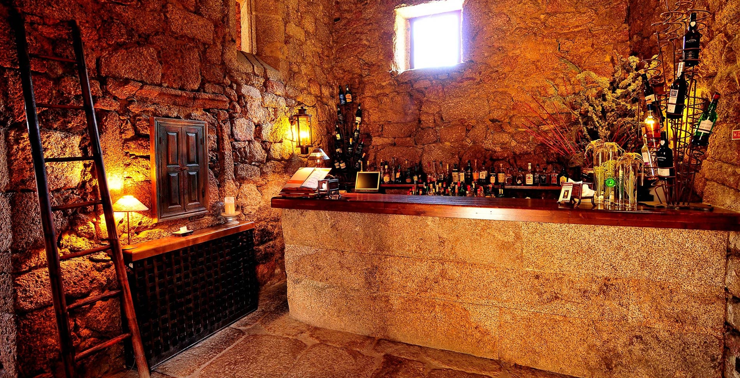 Bar de la Pousada Convento de Belmonte, con barra y varias botellas, algunas decorativas, otras para cocktails