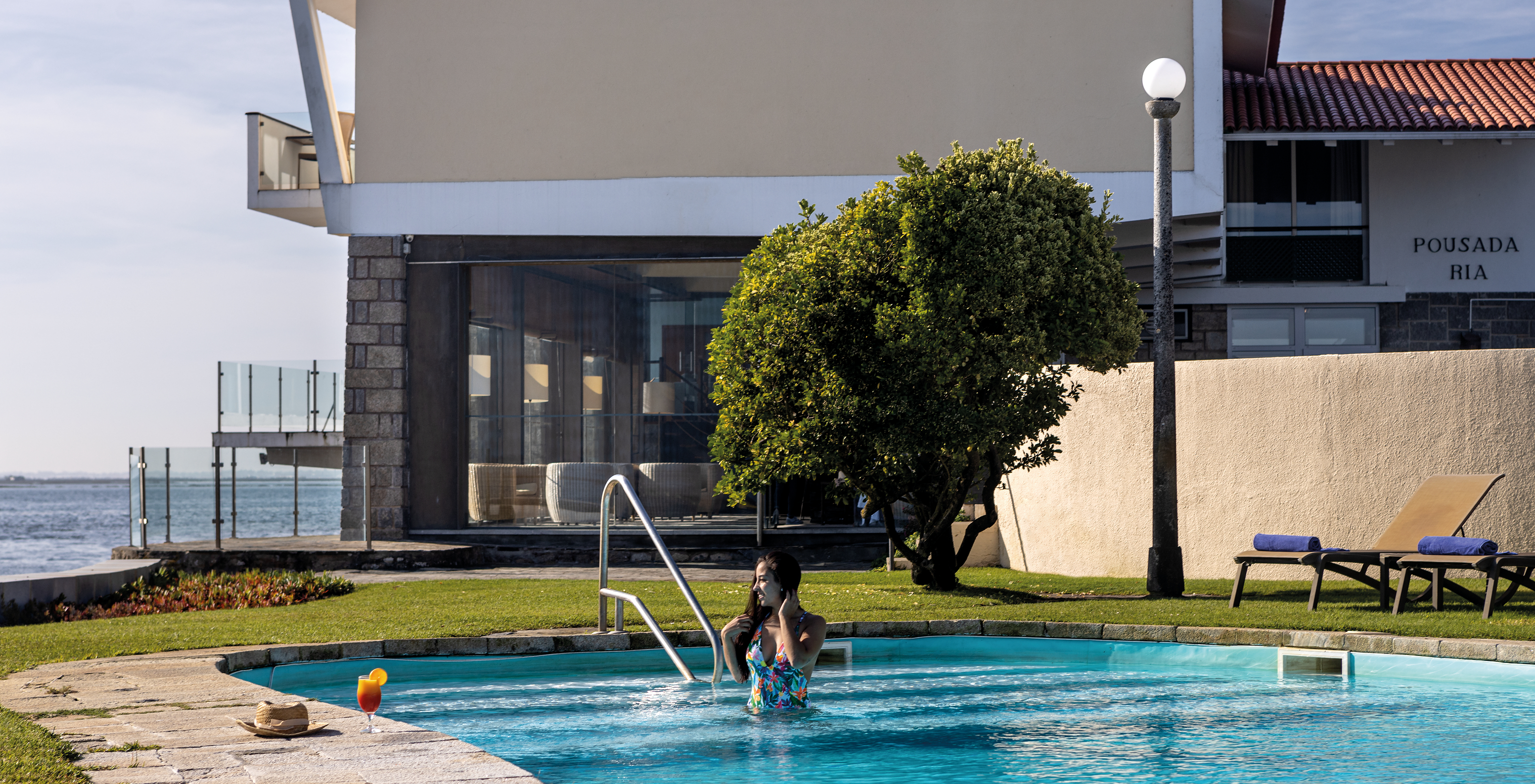 Persona en la piscina bebiendo un cóctel con la fachada de la Pousada Ria - Aveiro al fondo