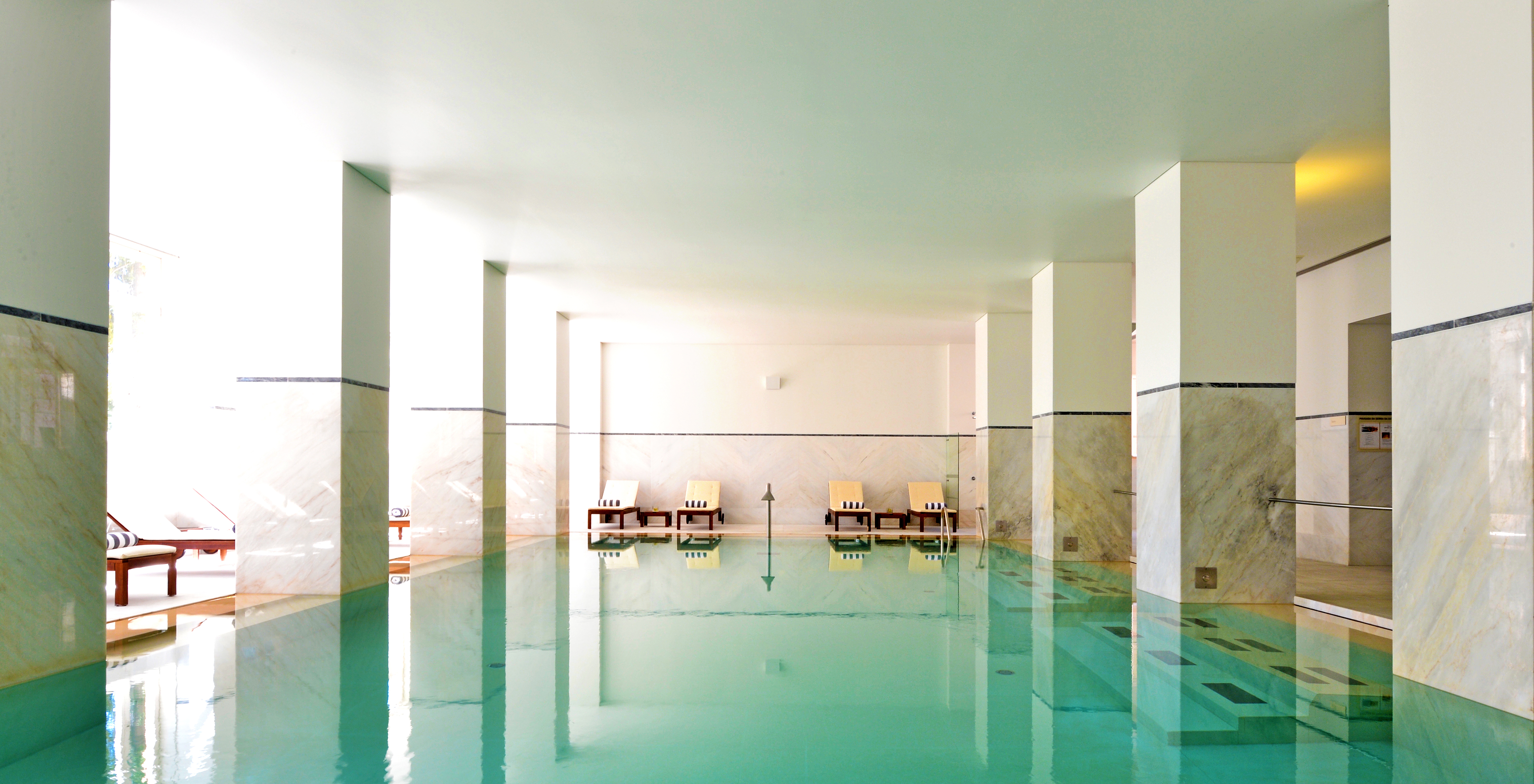 Piscina interior en hotel de montaña en el centro de Portugal con tumbonas con toallas enrolladas al fondo