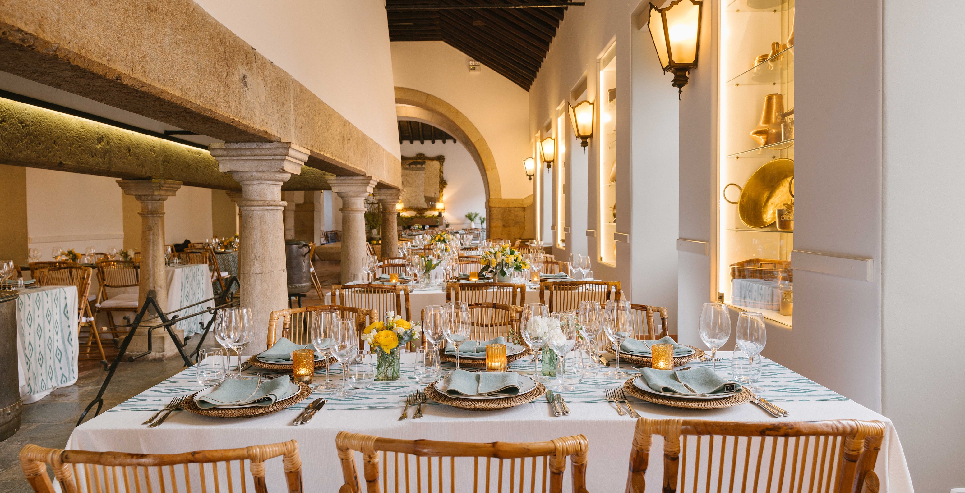 Cocina antigua transformada en sala de eventos con mesas redondas puestas con servicio completo de comida