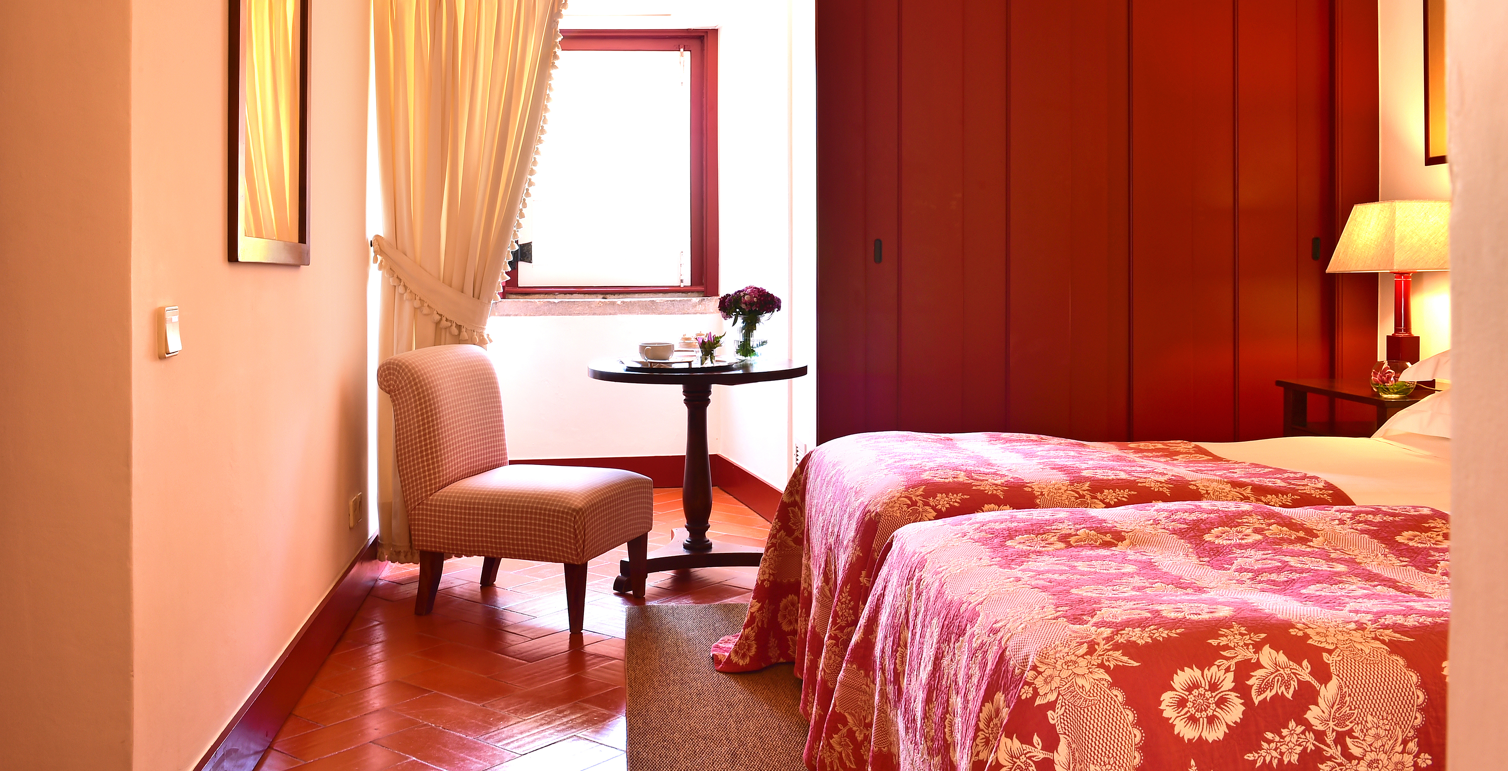 The Classic Room of The Pousada Convento Beja has a side table with a chair by the window of the room