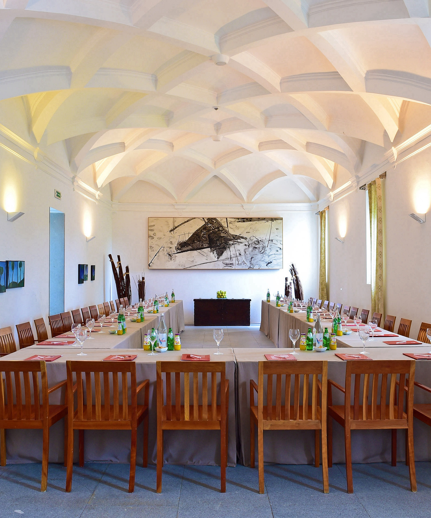 Vergaderzaal van de Pousada Convento Arraiolos, met een grote tafel met stoelen en drankjes, en drie ramen met gordijnen