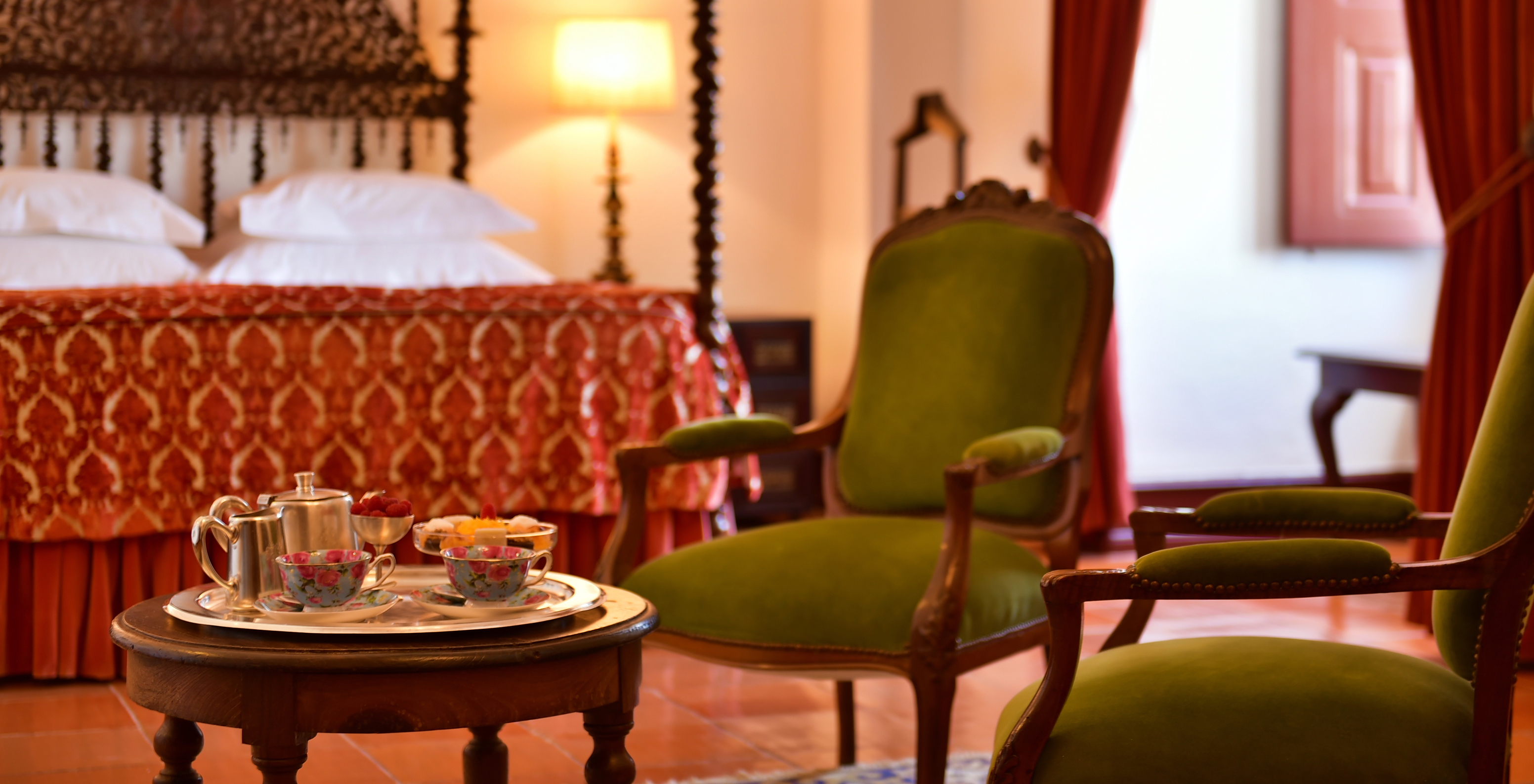 A Junior Suite da Pousada Castelo Estremoz tem duas cadeiras verdes almofadadas, com uma mesa em frente com um lanche montado