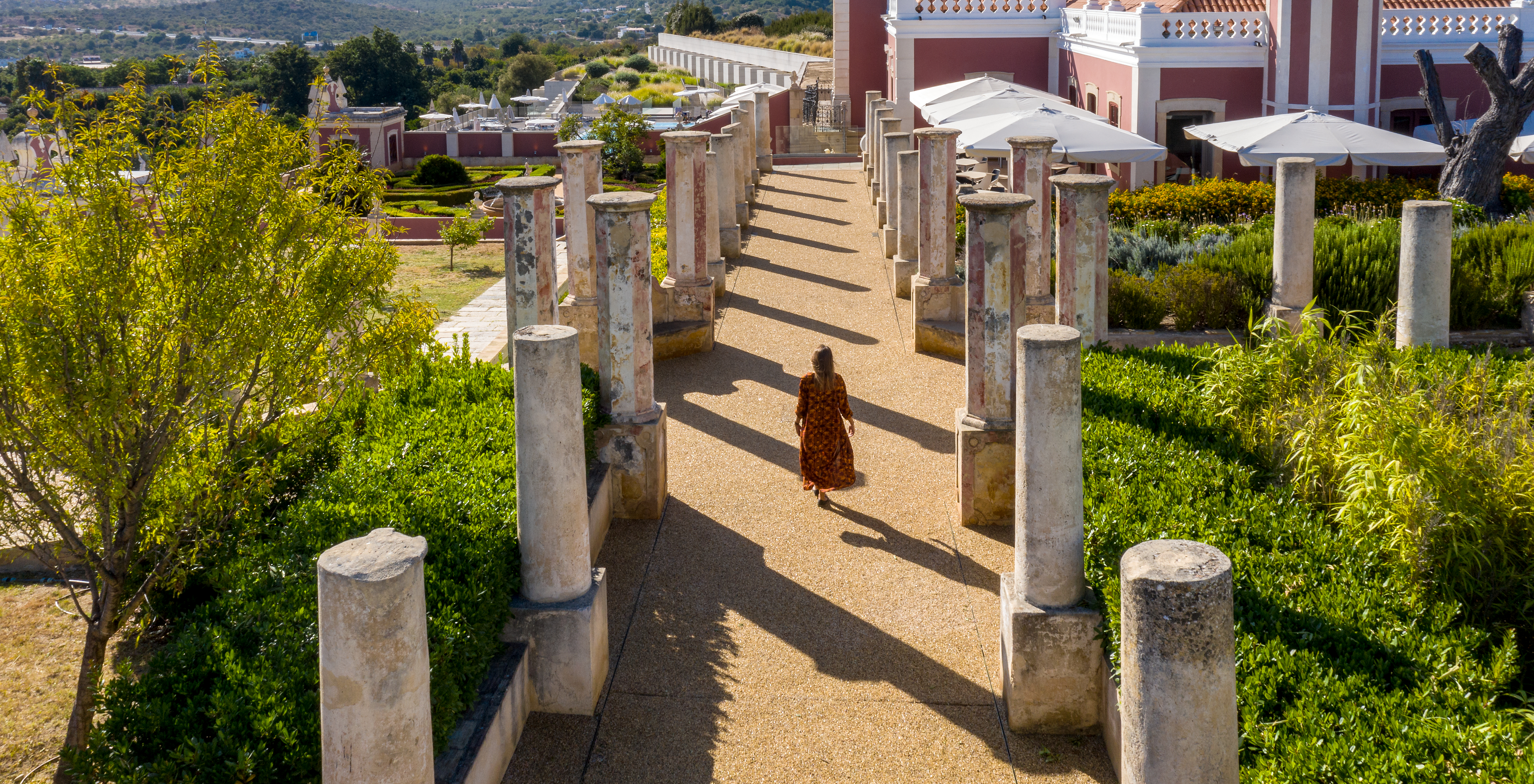 Rapariga a passear entre os pilares de pedra da Pousada Palácio Estoi, Hotel Histórico em Faro, e o edifício ao fundo