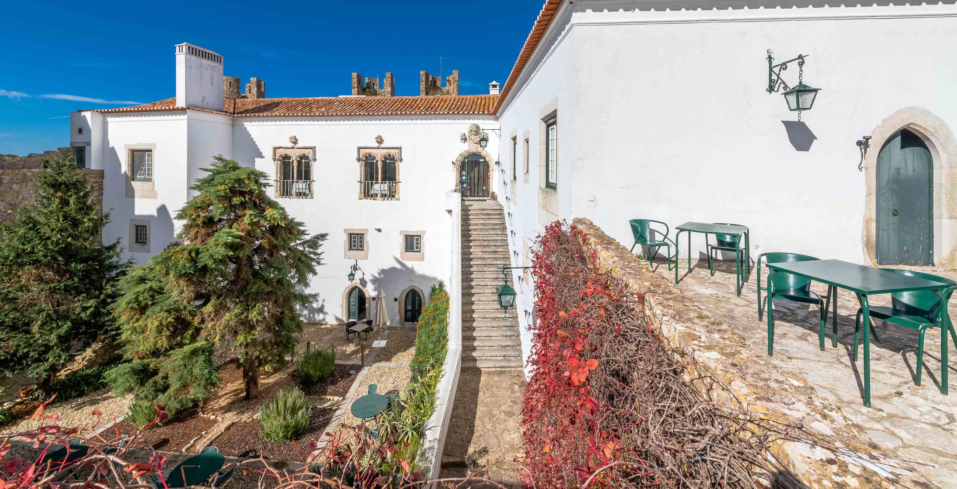 Vista exterior do edifício da pousada, com uma escadaria para o jardim e uma pequena esplanada com mesas e cadeiras verdes