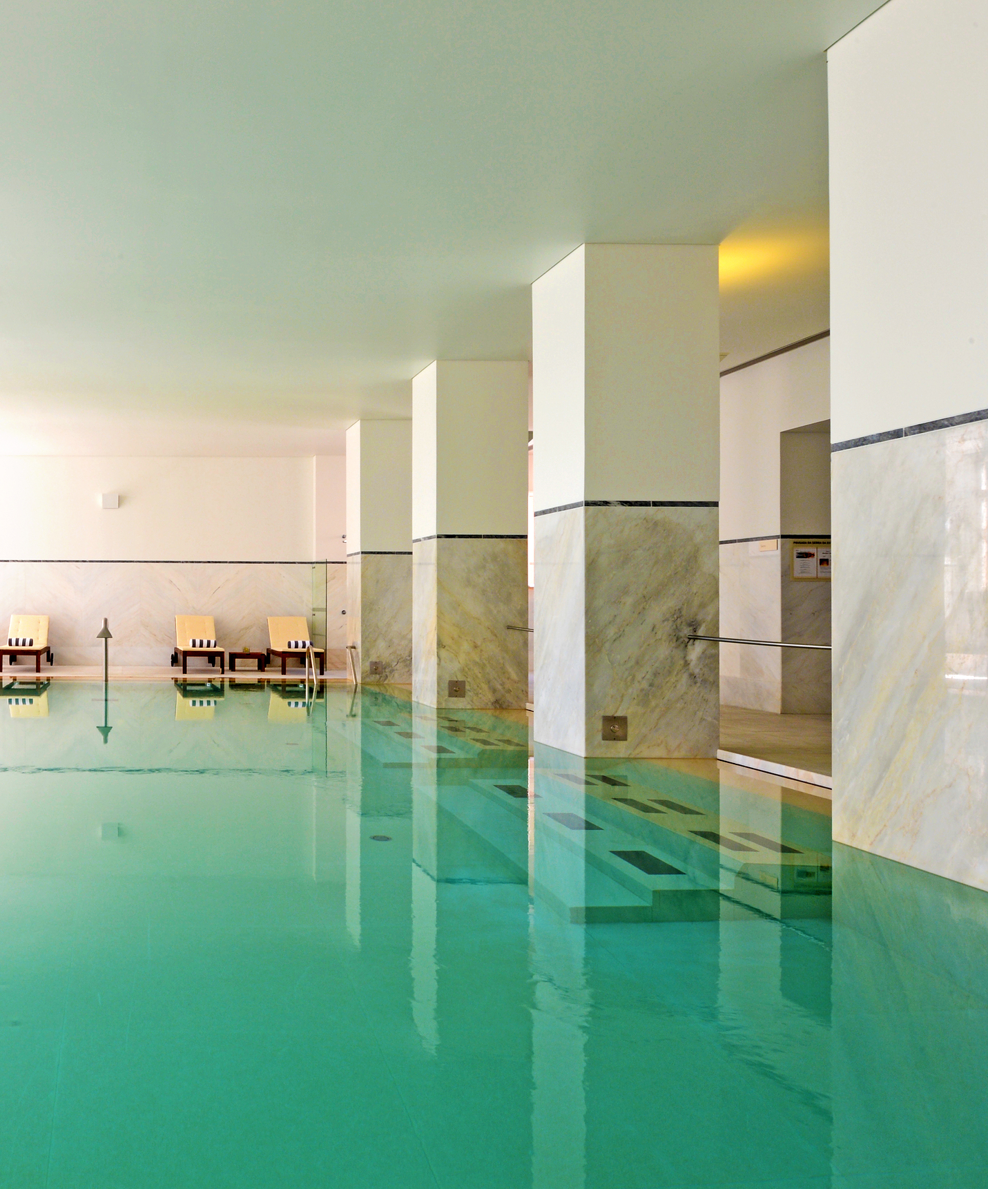 Piscina interior em Hotel de Montanha no Centro de Portugal, com espreguiçadeiras com toalhas enroladas ao fundo