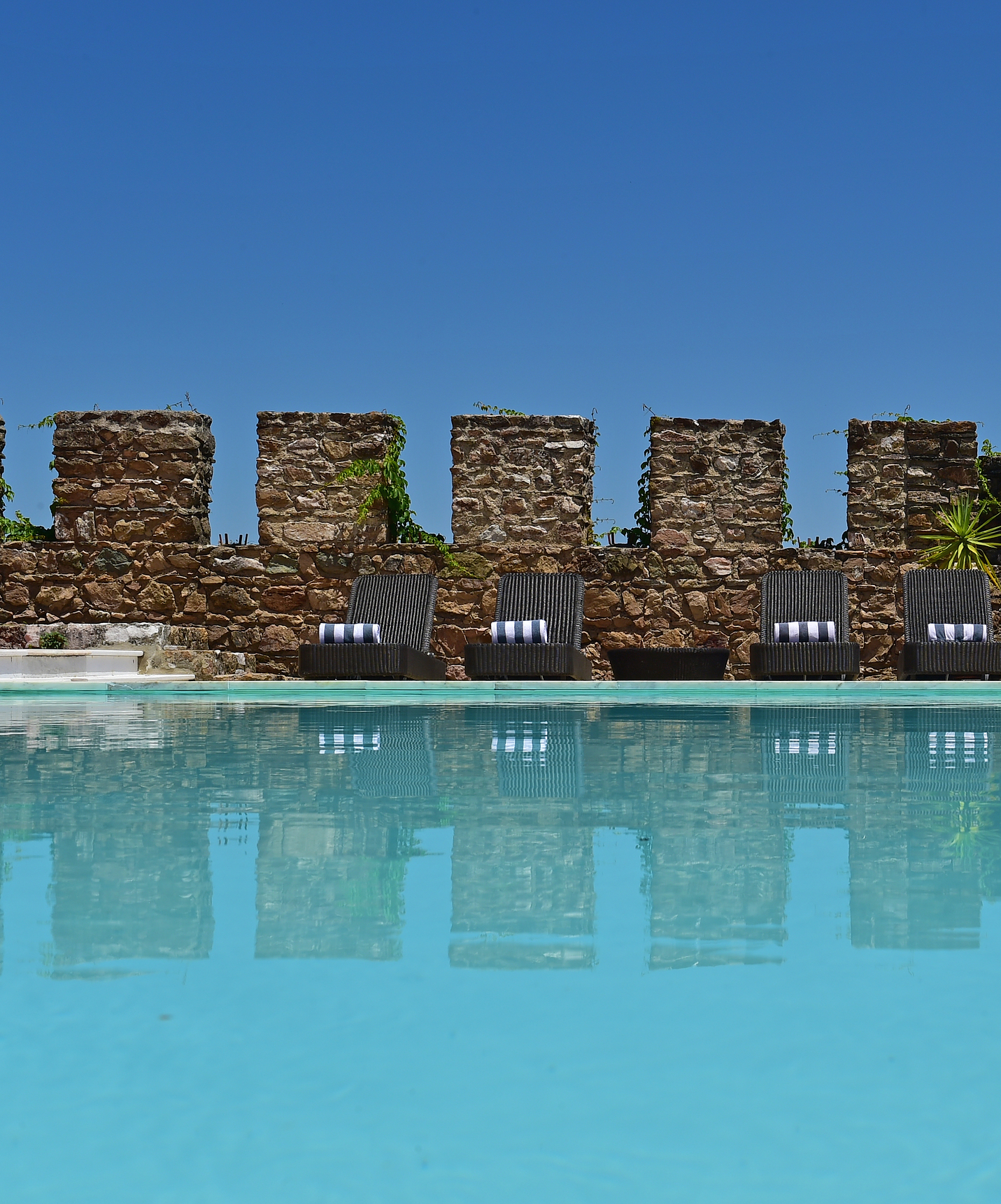 Vista da piscina exterior do hotel no Centro Histórico de Estremoz, com espreguiçadeiras, cercada por uma muralha