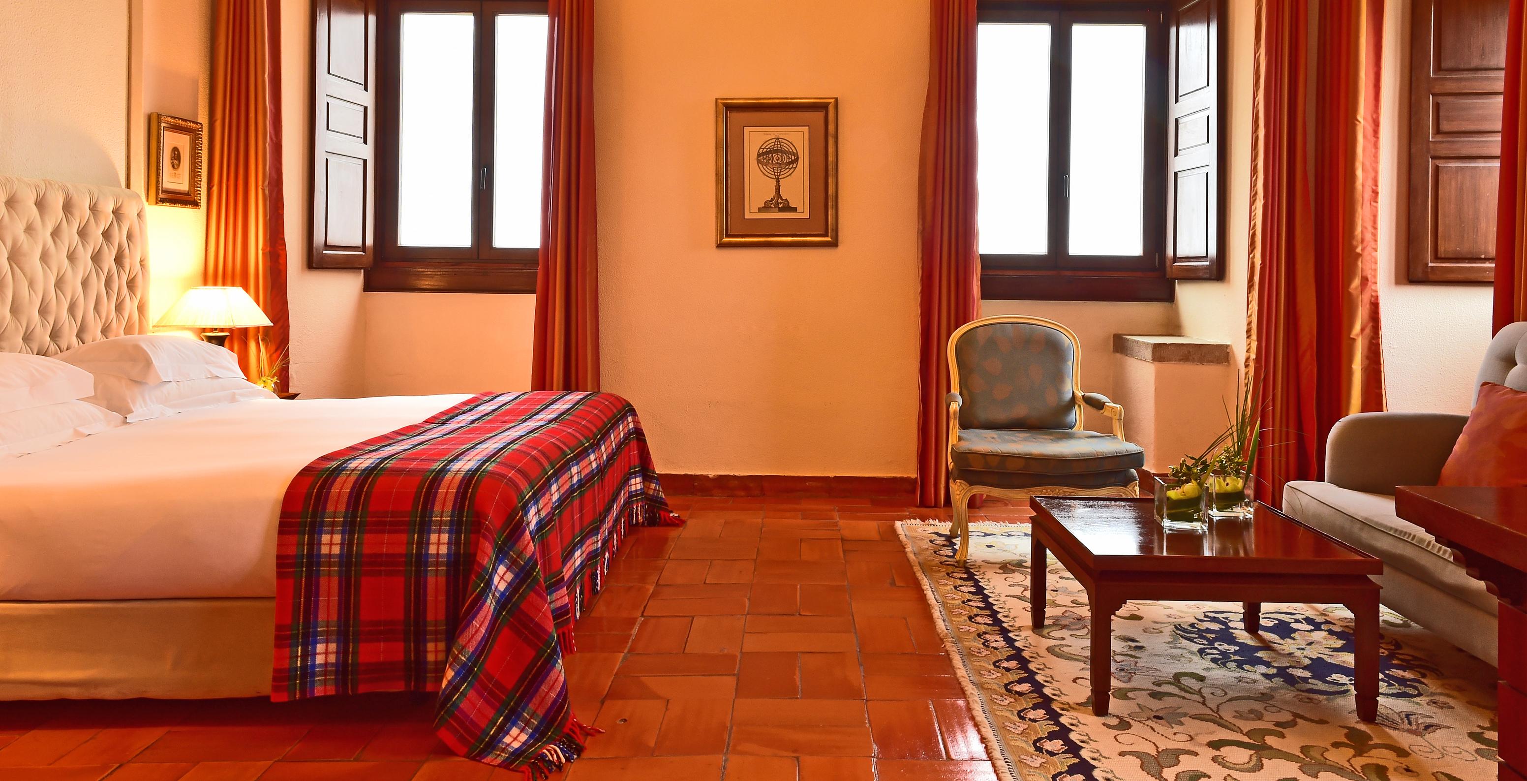 A Master Suite da Pousada Castelo Palmela tem uma cama de casal, duas janelas, um sofá, uma poltrona e uma mesa em madeira